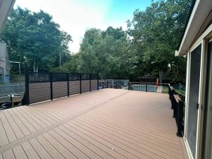 A spacious wooden deck with decorative privacy panels overlooks a backyard with trees and a fence, next to a house with large sliding glass doors.
