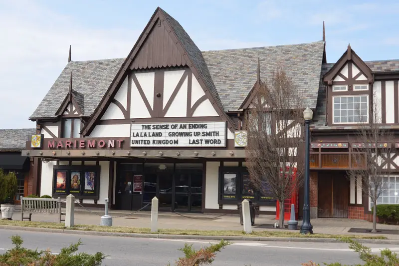 A Tudor-style cinema with a marquee reading “THE SENSE OF AN ENDING, LA LA LAND, GROWING UP SMITH, UNITED KINGDOM, LAST WORD.” The building has steep roofs, dark trim, and a sign that says MARIEMONT.